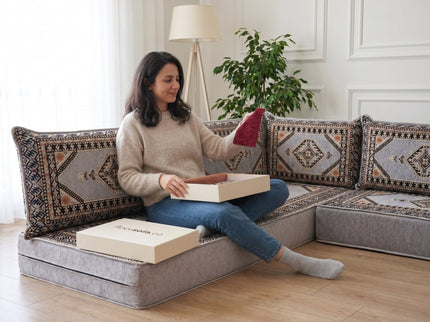 Woman on a gray floor sofa comparing a maroon fabric swatch from the sample box